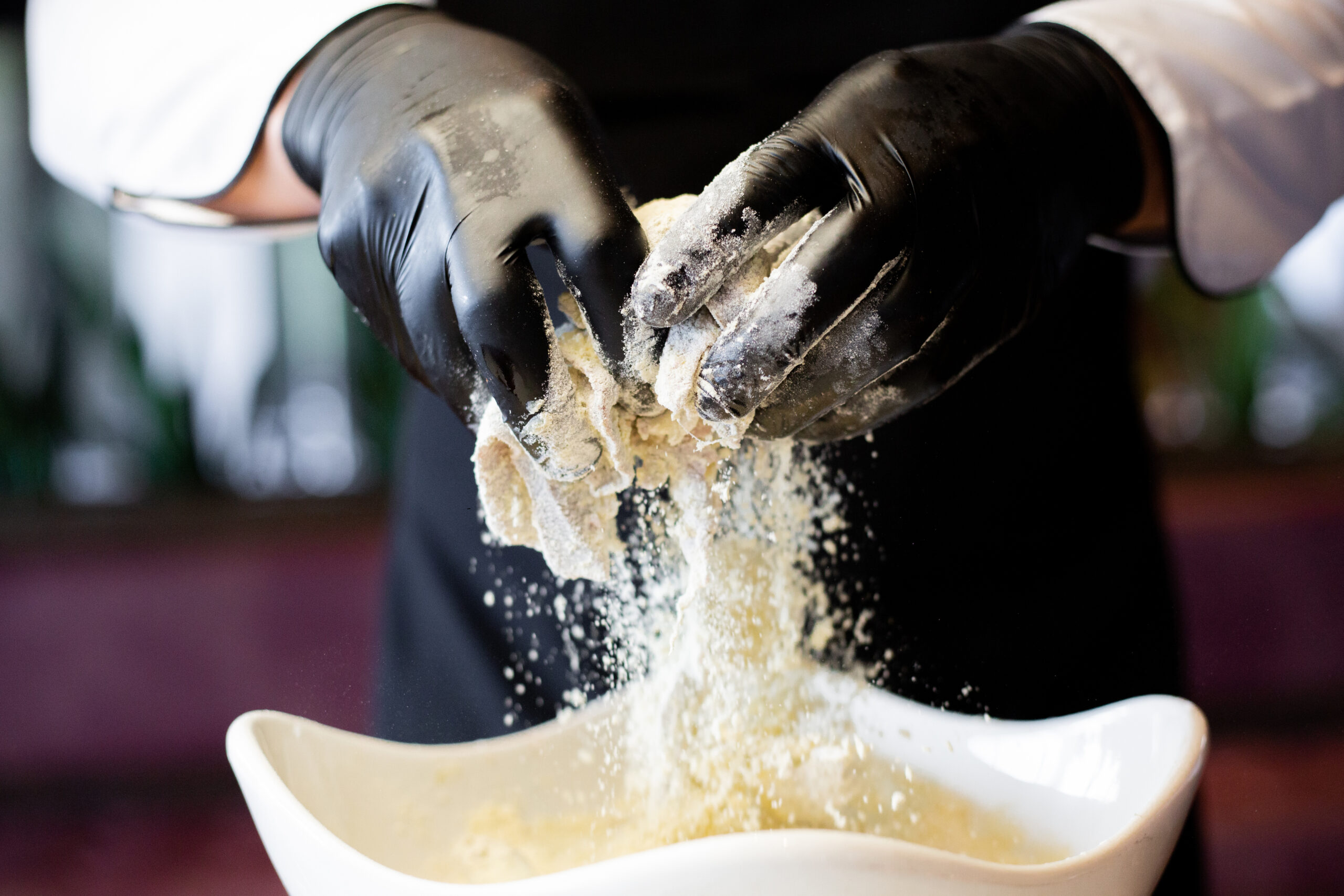 chef hands are flouring the meat in a bowl before frying it.